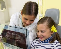 Young Dentist showing a girl an x-ray of her teeth | Preventative Orthodontics for Kids | Alluring Smiles in Mesa, AZ - Dr. Javier Portocarrero